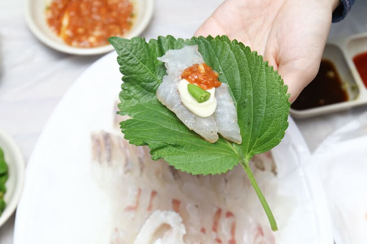 Hand holding Hoe, a Korean Raw fish sashimi.