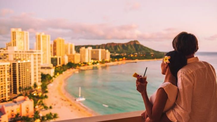 Hawaii luau vacation Mai Tai drink cocktail couple tourists at Honolulu hawaiian resort hotel. Happy man and woman relaxing at sunset view of Diamond Head